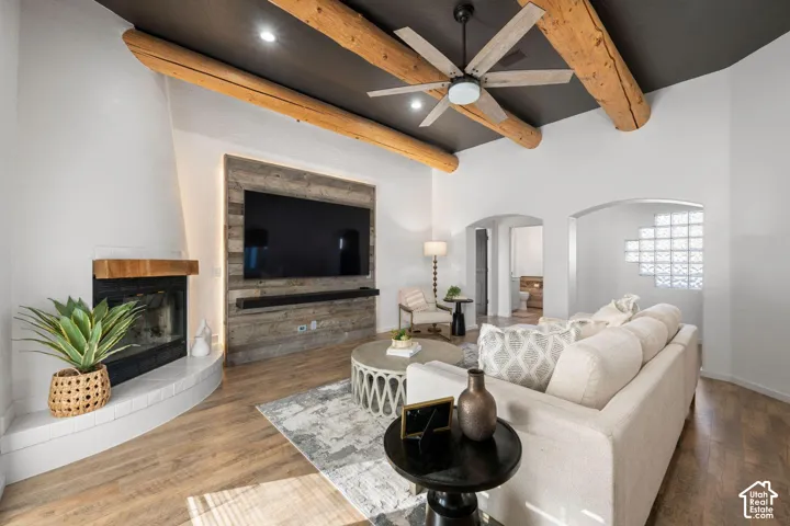 Living space featuring exposed timber beams, a dark-toned vaulted ceiling, a wood-paneled media wall with integrated lighting, a fireplace with a wood mantel, and glass block accent windows