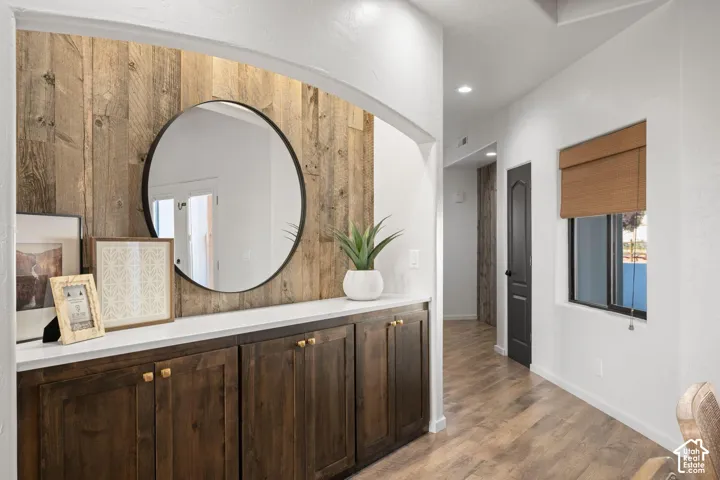 Built-in cabinetry with dark wood finish, white countertop, vertical wood-plank wall accent, circular mirror, and recessed lighting