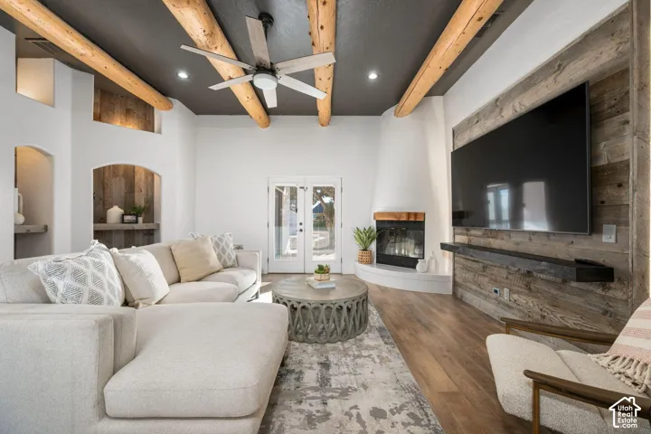 Living area featuring exposed log ceiling beams, a wood-paneled accent wall, a floor-to-ceiling fireplace with a wood mantel, wood-finish flooring, and recessed architectural niches