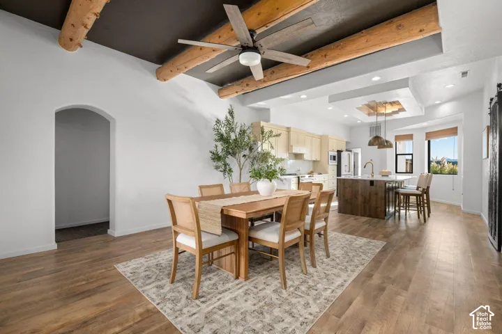 Exposed log ceiling beams, wood-finish flooring, recessed lighting, central island with dark wood cabinetry, and arched interior doorway