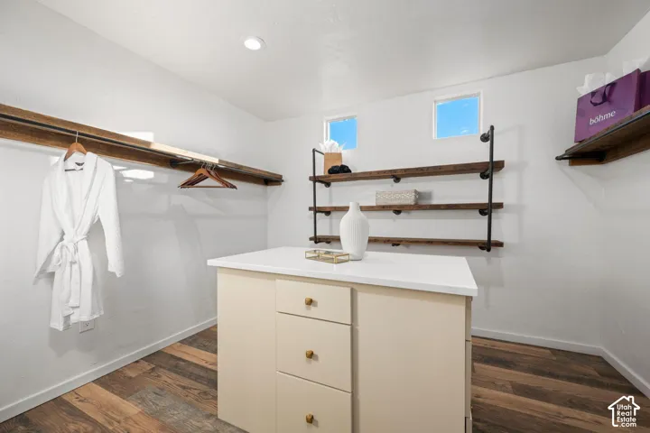 Walk-in closet featuring wood-finish flooring, a central island with a quartz countertop, industrial pipe shelving, recessed lighting, and dual high-set windows