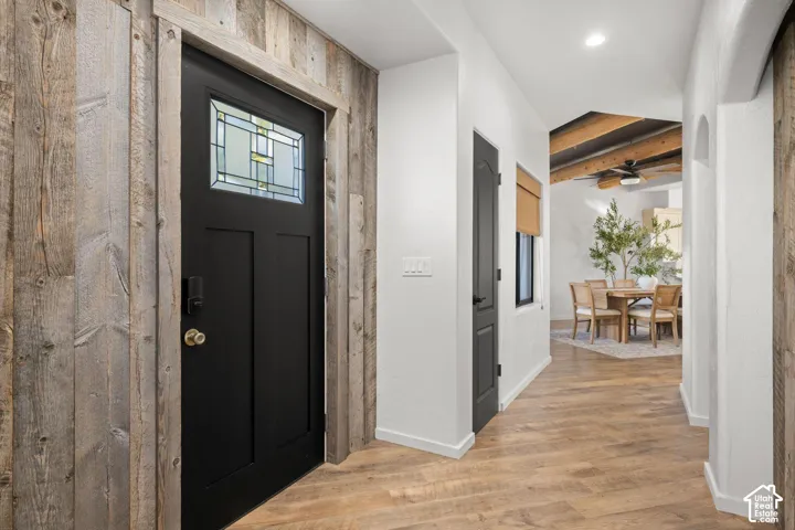 Entryway featuring reclaimed wood wall paneling, a black paneled door with a leaded glass insert, wood-finish flooring, and exposed ceiling beams