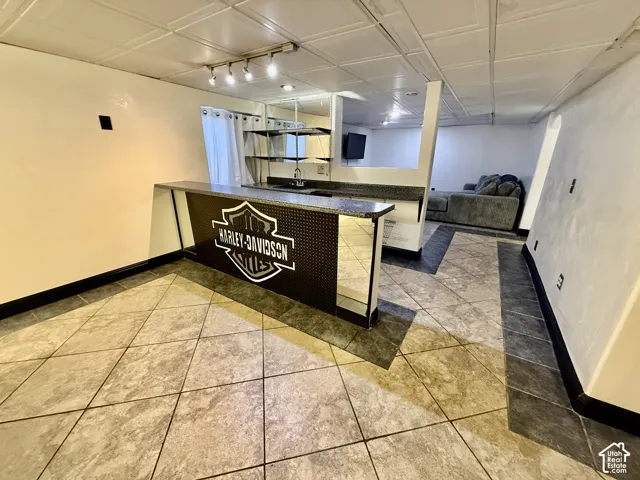 Built-in wet bar featuring a stone-finish countertop, stainless steel sink, tile flooring with decorative borders, and multi-directional track lighting