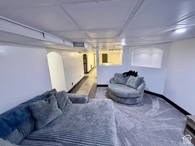 Finished interior space featuring a grid-pattern drop ceiling, recessed lighting, a recessed wall niche, arched doorways, and a combination of carpet and tile flooring