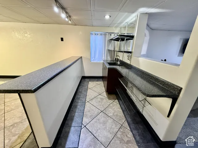 Bar area featuring a dual-level countertop, inset sink, built-in metal shelving, and decorative tile flooring