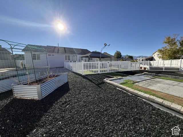 Backyard featuring a white vinyl fence, metal-sided raised garden beds, a metal-framed gazebo, and stone-bordered landscaping