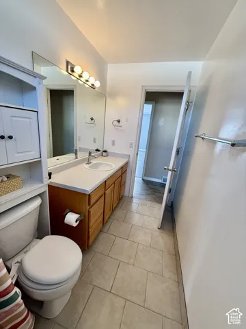 Bathroom featuring large-format tile flooring, wood cabinetry, a solid surface countertop with an integrated basin, wall-to-wall vanity mirror, and multi-bulb fixed lighting