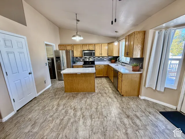Kitchen featuring light wood cabinetry, stone-finish countertops, stainless steel appliances, a central island, and tile flooring