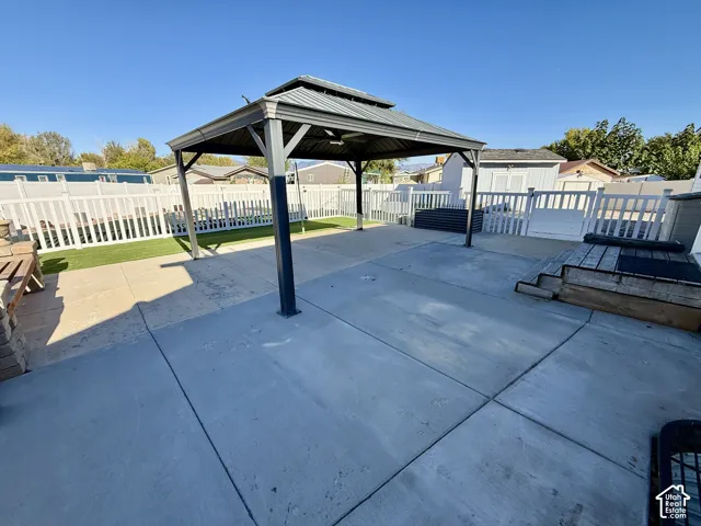 Concrete patio featuring a metal-frame gazebo with a dual-tiered roof, fully fenced perimeter with white vinyl panels, and an artificial turf lawn