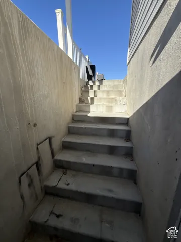 Concrete exterior staircase featuring poured concrete retaining walls and a white vinyl railing