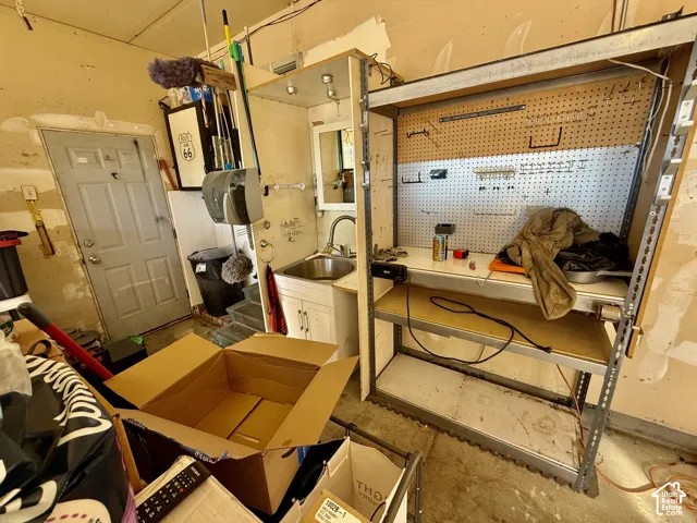 Utility area featuring a stainless steel drop-in sink, white cabinetry with silver-tone hardware, and an integrated metal workbench with a perforated tool board