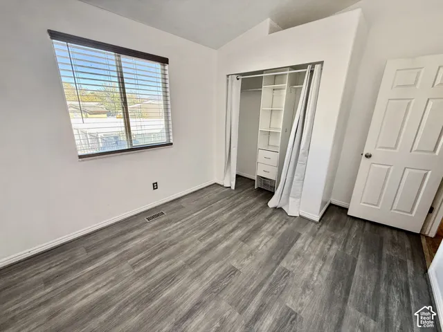 Room featuring wood-finish flooring, a window with horizontal blinds, and a built-in closet system with shelving and drawers