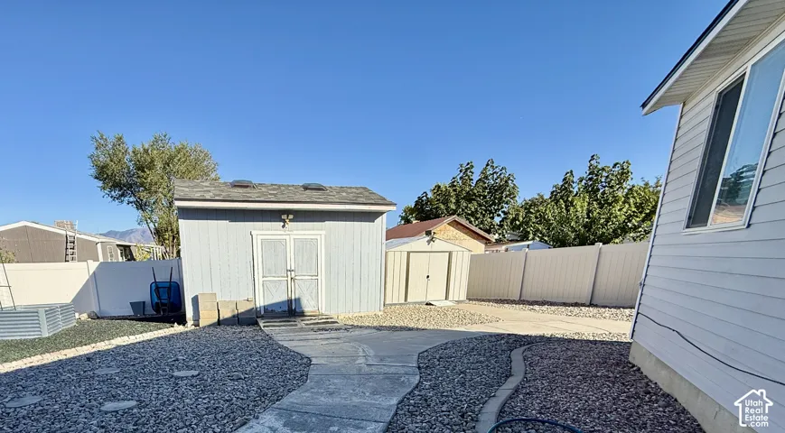 Low-maintenance gravel landscaping featuring a concrete pathway, privacy fencing, and two detached storage structures