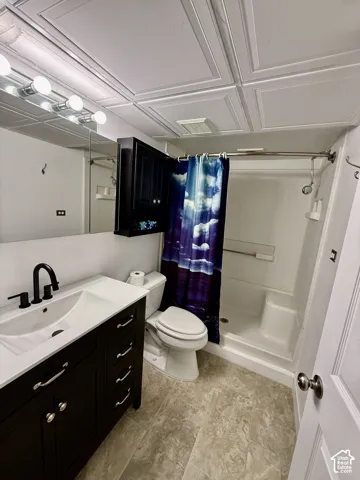 Bathroom featuring a vanity with a white countertop and matte black faucet, dark cabinetry, tile-patterned flooring, and a walk-in shower with integrated shelving