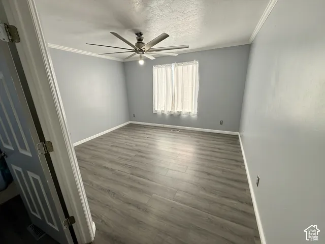Room featuring wood-finish flooring, crown molding, and a multi-blade ceiling fan