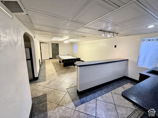 Large room featuring a drop ceiling, tile flooring, a built-in counter with a dark solid-surface top, and integrated track lighting