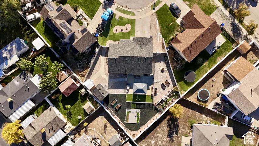 Aerial perspective of a property featuring extensive paver hardscaping, built-in raised garden beds, a covered patio structure, and a fenced backyard