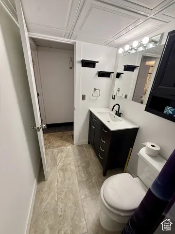 Bathroom featuring a vanity with dark cabinetry, a white integrated countertop and sink, matte black faucet, wall-mounted floating shelves, and tile flooring