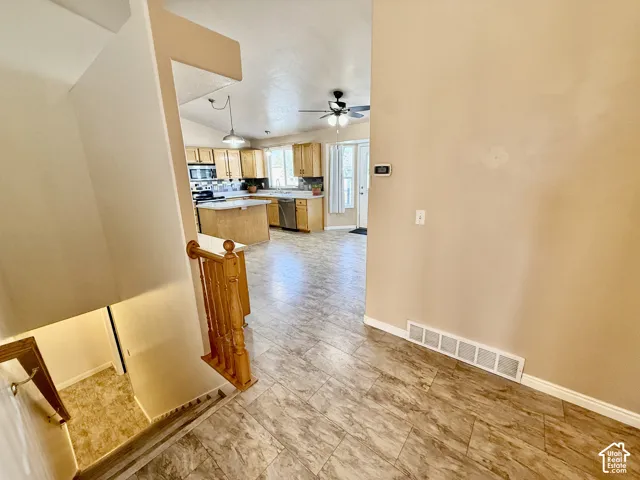 Kitchen featuring wood cabinetry, an island with countertop seating, tiled flooring, and a ceiling fan with integrated lighting