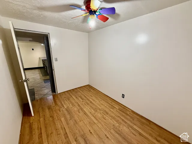 Room featuring wood-finish flooring, a multi-colored ceiling fan, and a neutral wall finish