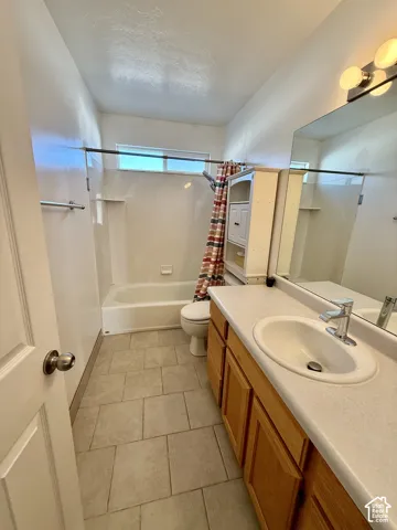 Bathroom featuring neutral tile flooring, a single-sink vanity with a solid-surface countertop, a wall-mounted mirror, and a tub-shower combination