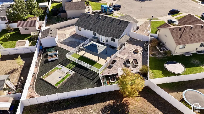 Expansive backyard featuring a fenced perimeter, stone-paved patio, synthetic turf area, and multiple raised garden beds
