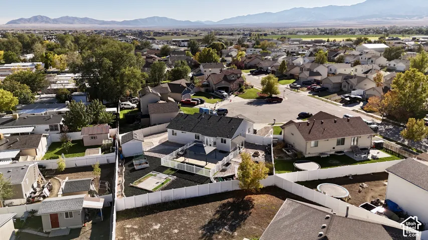 Aerial perspective of a fenced backyard featuring a paved patio, a white vinyl perimeter fence, a detached storage shed, and a mountain backdrop
