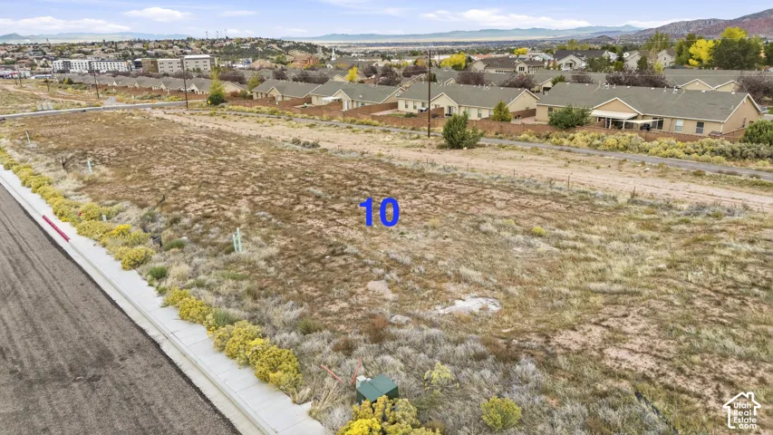Expansive corner lot featuring paved street access, concrete sidewalk, utility connection, and distant mountain backdrop