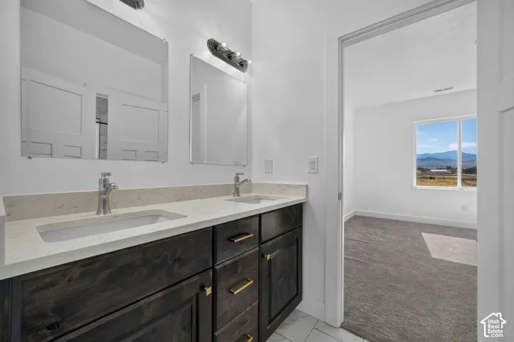 Dual-sink vanity with stone-finish countertop, dark wood-finish cabinetry, polished metal hardware, and dual wall-mounted mirrors