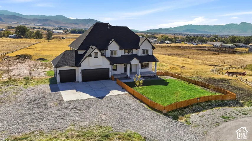 Multi-story residence featuring a dark shingled roof, a three-car garage, an enclosed lawn area, and a prominent mountain backdrop