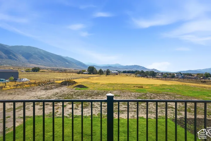 Black metal railing overlooking an expansive open field, mature trees, and a mountain range backdrop