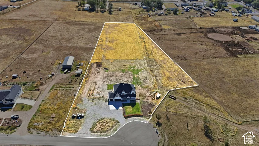 Aerial perspective of a multi-acre parcel featuring an expansive lot, a residence with a multi-gabled roofline, and a gravel driveway providing access to the structure