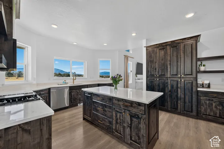 Kitchen featuring stained wood cabinetry, a central island with a stone-composite countertop, stainless steel appliances, recessed lighting, and wood-finish flooring
