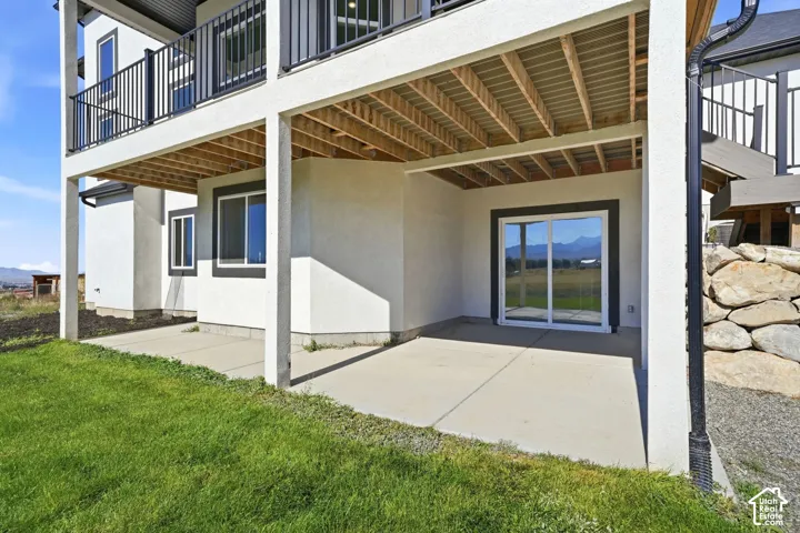 Covered concrete patio featuring a sliding glass door, upper-level balcony with metal railing, and decorative stone retaining wall