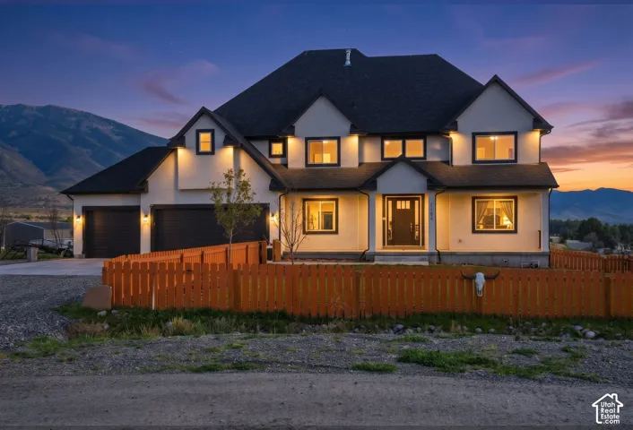 Two-story residence featuring a multi-gabled roofline, stucco exterior, three-car garage, and mountain backdrop