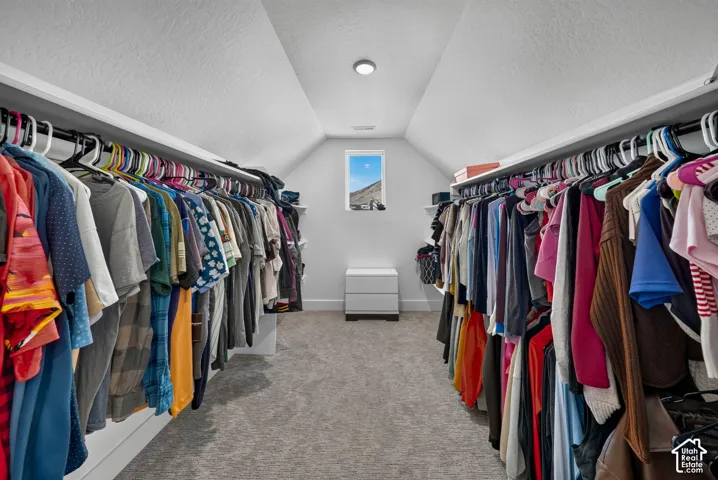Walk-in closet featuring vaulted ceilings, wall-to-wall carpeting, dual-sided tiered hanging rods, and a center window