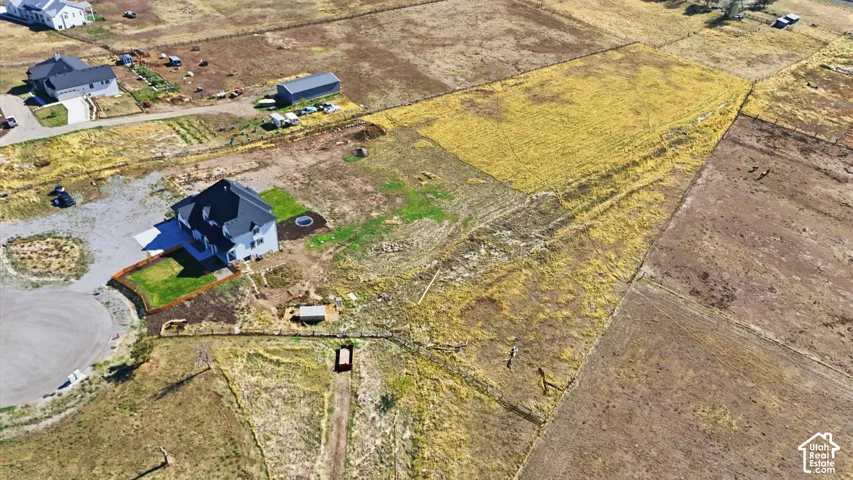 Aerial perspective of a multi-story residence with a dark-toned roof, paved driveway, dedicated lawn space, and extensive open acreage
