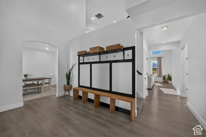 Built-in mudroom bench with paneled backing and integrated coat hooks, wood-finish flooring, vaulted ceiling, recessed lighting, and arched doorways