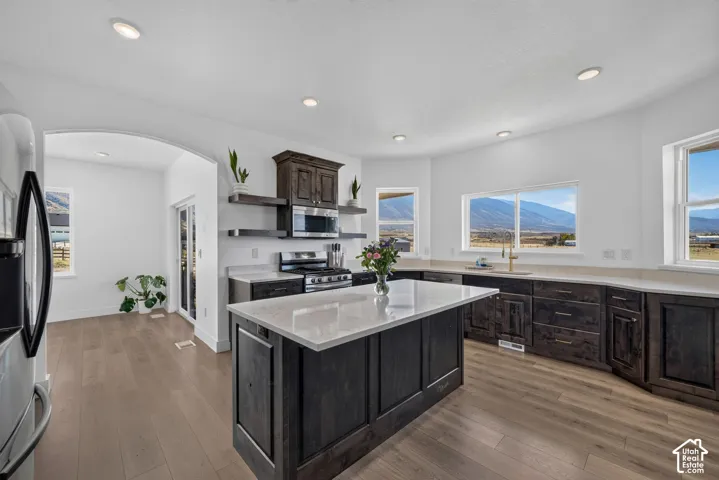 Kitchen featuring dark wood-finish cabinetry, central island with stone-finish countertop, floating wood shelving, recessed lighting, and expansive windows
