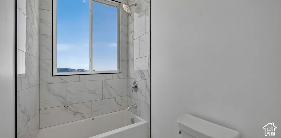 Full-height shower surround featuring large-format stone-patterned tile, integrated soaking tub, chrome fixtures, and a single-hung window with dark trim