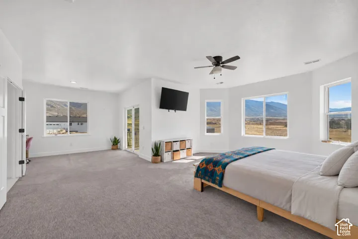 Spacious bedroom featuring wall-to-wall carpeting, multiple windows with mountain scenery, a central ceiling fan, and a glass-paned door