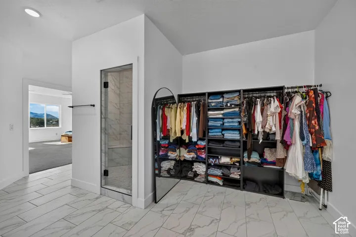 Walk-in shower featuring glass door enclosure and full-height stone-finish tile surround, complemented by stone-finish tile flooring and recessed lighting