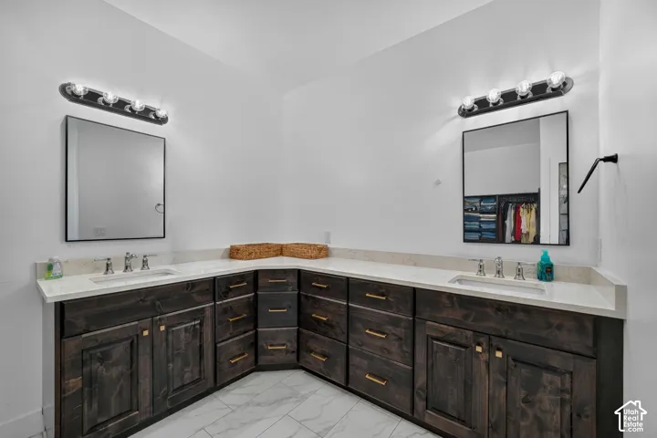 L-shaped wooden vanity with dark finish, dual undermount sinks, stone-finish countertops, dual wall-mounted mirrors with black frames, and tiled flooring
