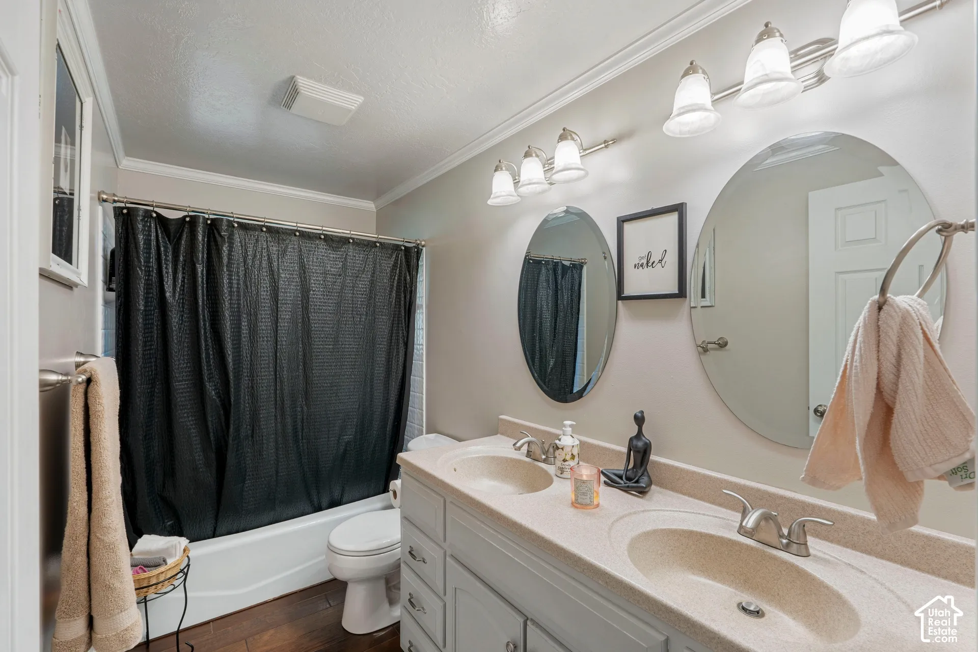 Dual-sink vanity with a solid-surface countertop, twin oval wall-mounted mirrors, two triple-light fixtures, and wood-finish flooring