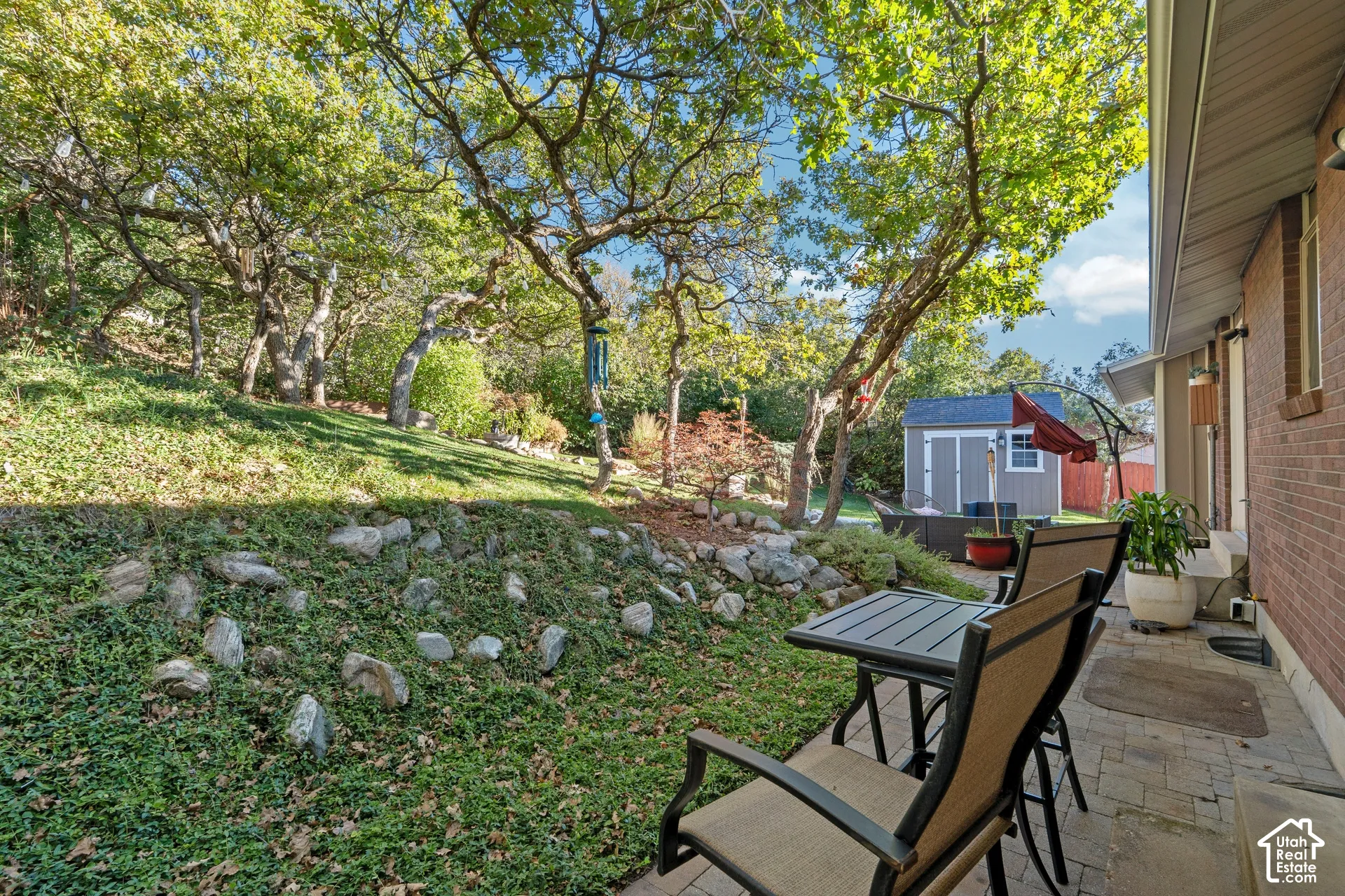 Brick exterior with a paved patio, terraced rock landscaping, and mature trees