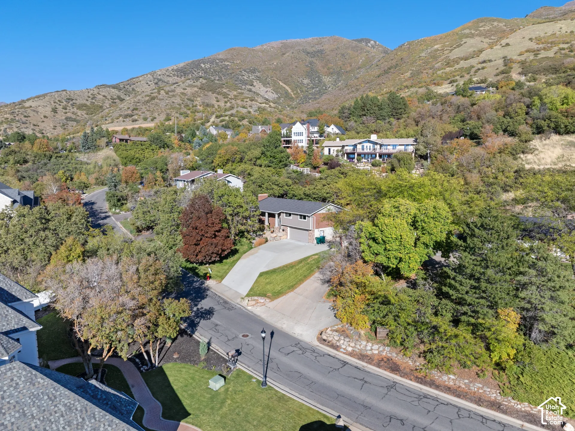 Residential property featuring a concrete driveway, attached garage, and mature tree-lined landscaping, set against a mountainous backdrop