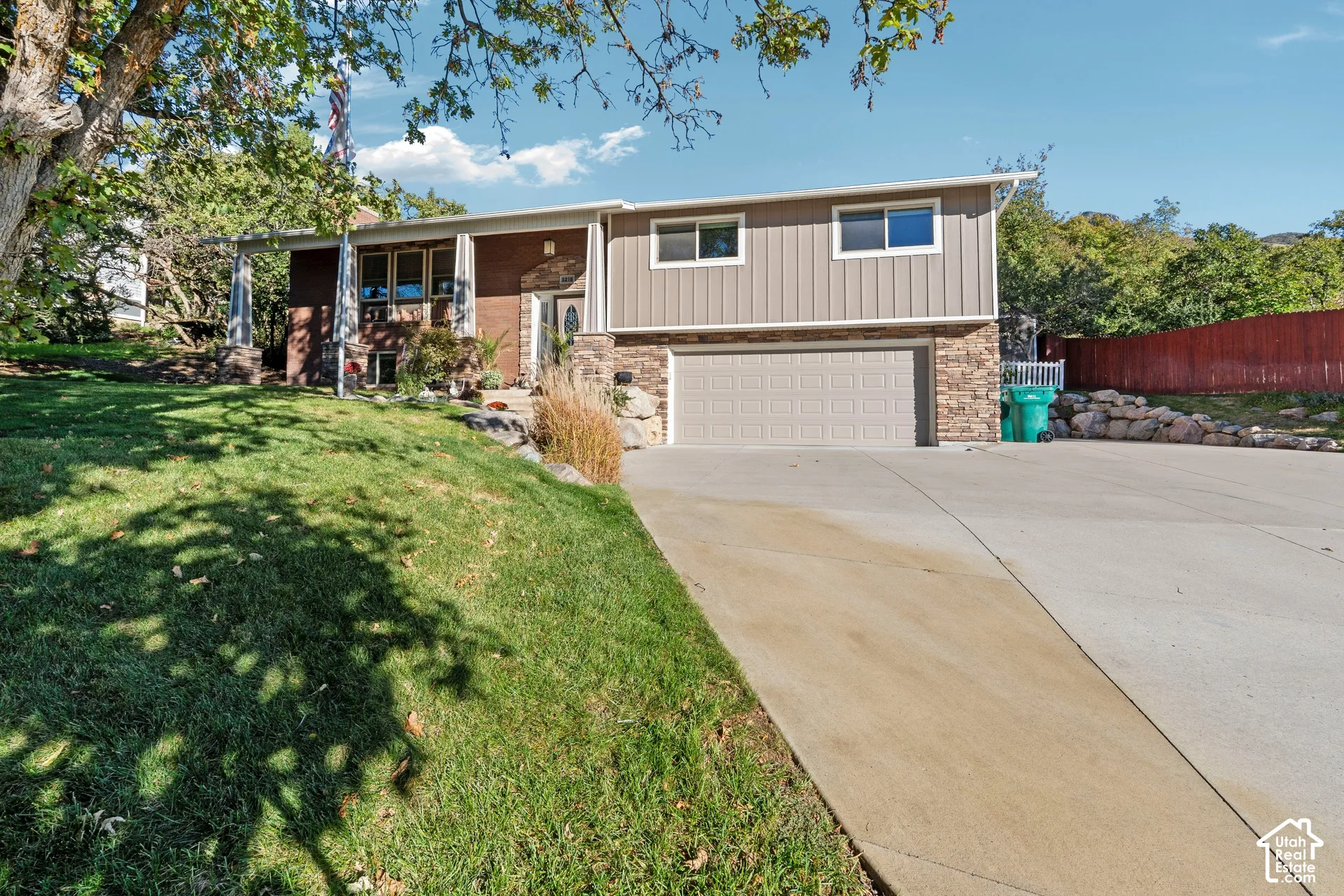 Multi-level exterior featuring a brick and stone facade, vertical metal siding, attached two-car garage, and concrete driveway