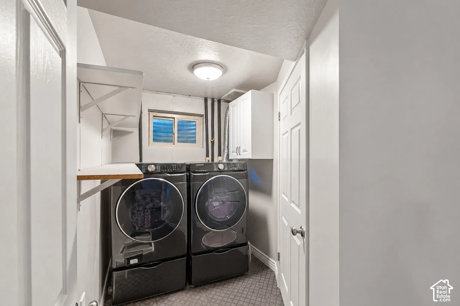 Dedicated laundry area featuring white wall-mounted cabinetry, custom open shelving, a recessed window, and a central ceiling light fixture