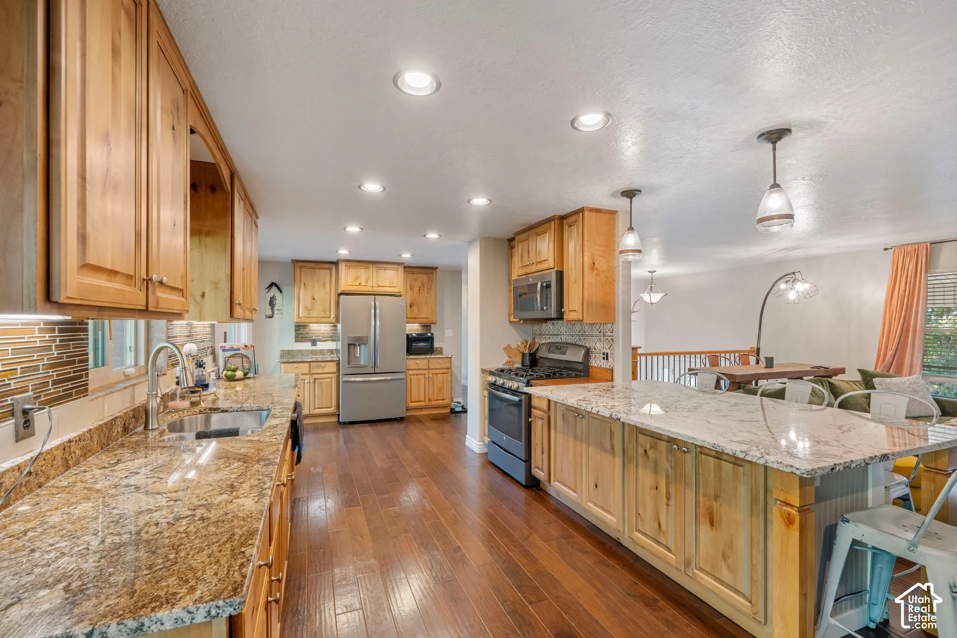 Kitchen featuring custom wood cabinetry, natural stone countertops, a large center island, stainless steel appliances, and wood-finish flooring