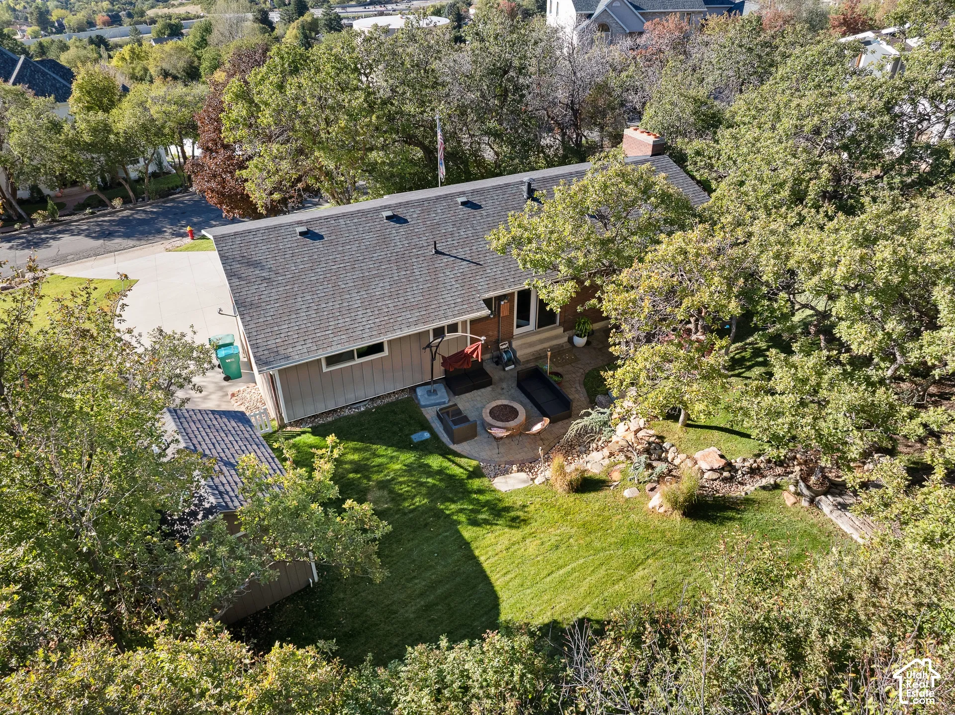 Aerial perspective featuring a shingled roofline, manicured lawn, stone-accented hardscaping, and mature trees